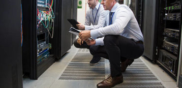 Computer technicians holding digital tablet while analysing server machines in server room.
