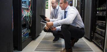 Computer technicians holding digital tablet while analysing server machines in server room.